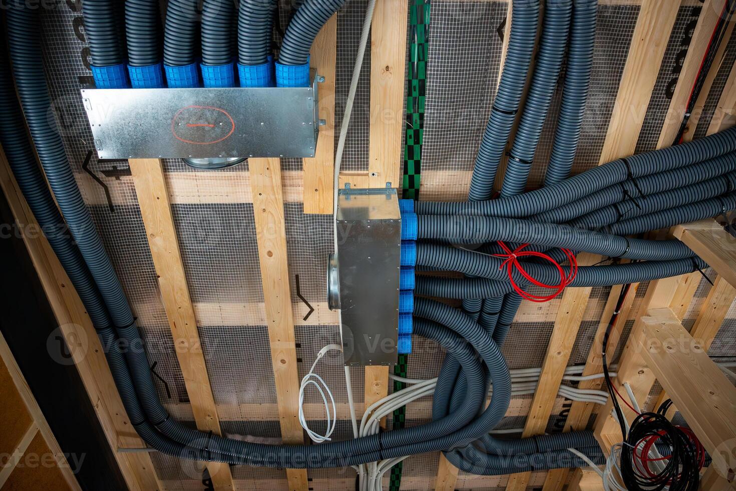 Interior view of house under construction featuring wooden beams, flexible ducts, metallic distribution boxes, and wiring for ventilation system. photo