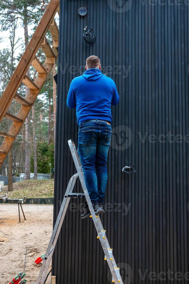Man on Ladder Working on Black Paneled Building at Construction Site photo