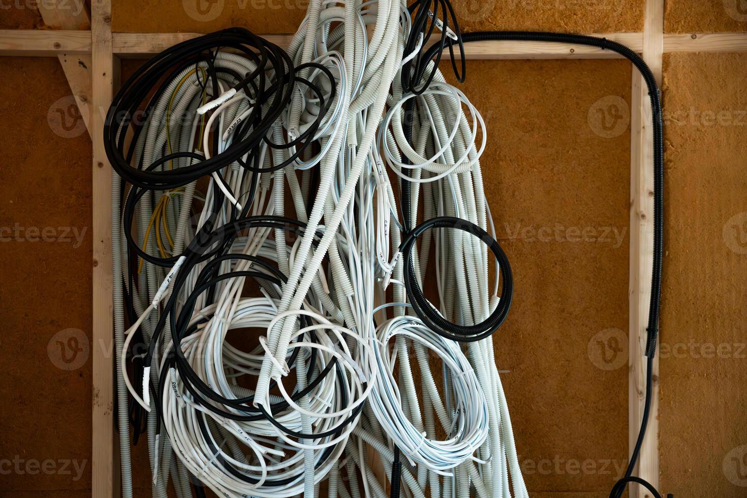 an Construction site interior showing coiled black and white conduits hanging on a wooden frame, with exposed studs and insulated walls in the background. photo