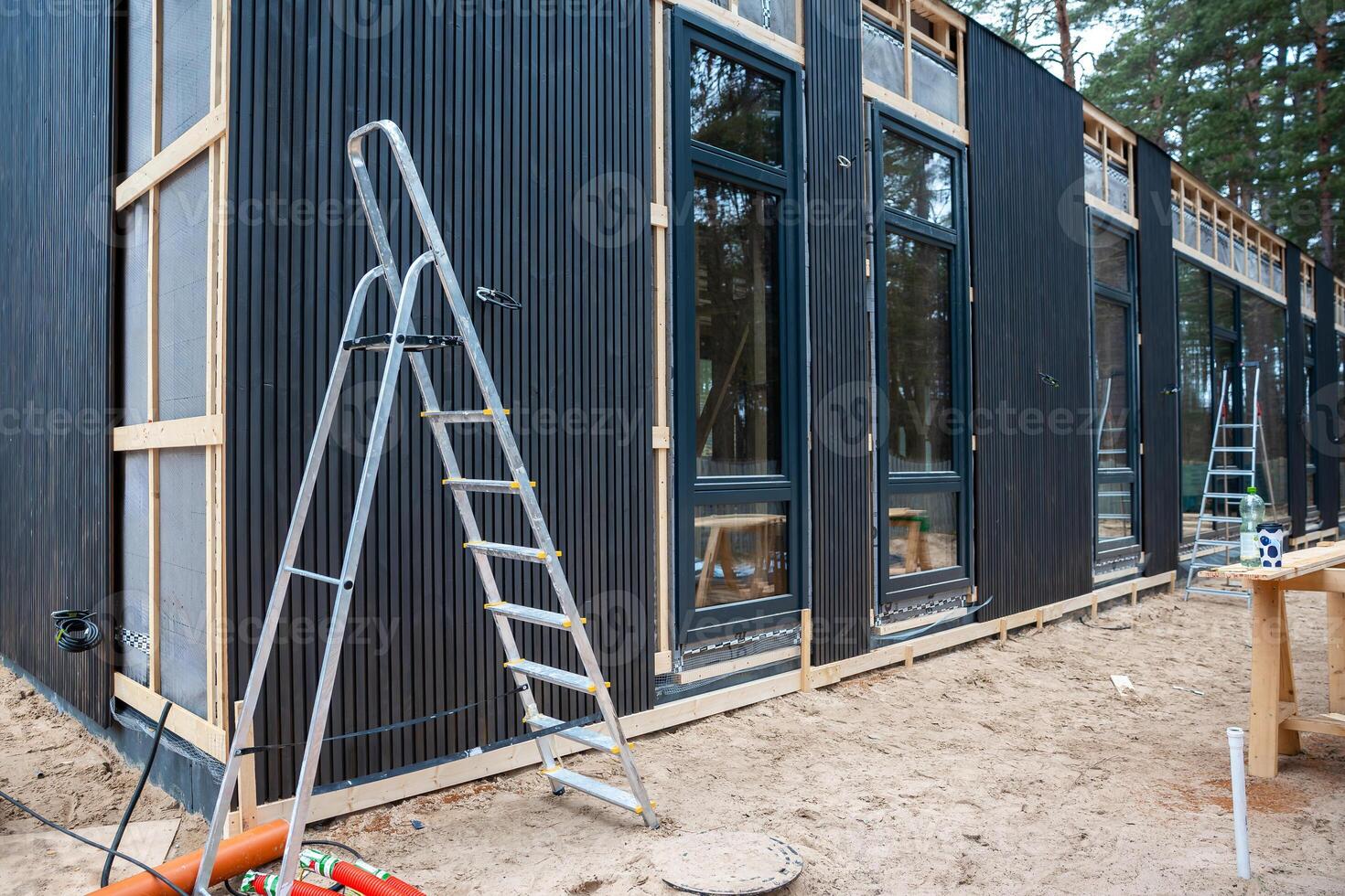Modern House Under Construction with Black Panel Exterior and Trees photo