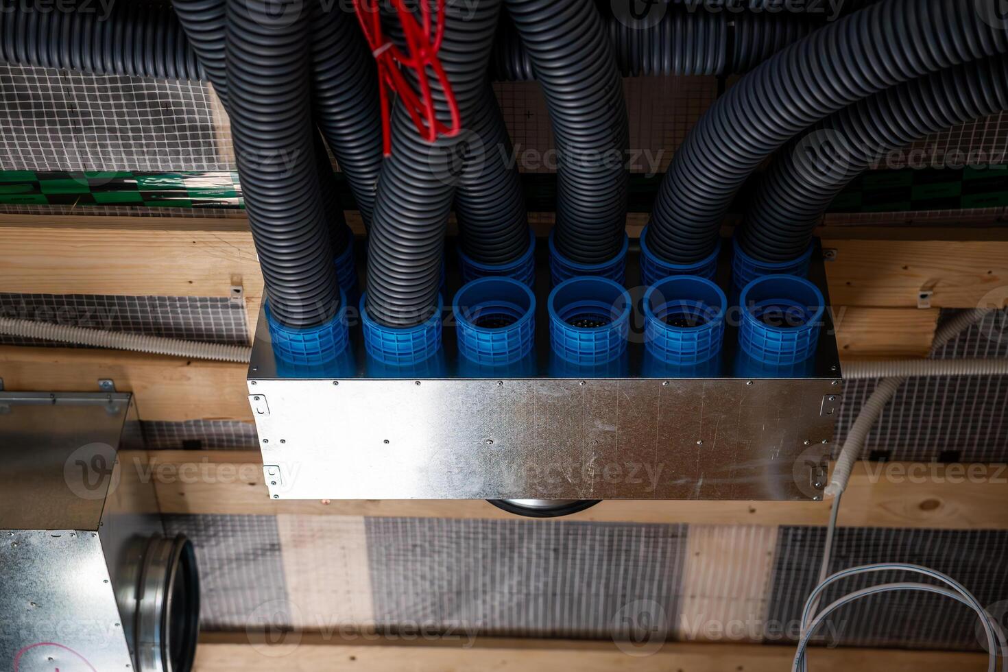 Section of a house under construction featuring a recuperation ventilation system with black ducts, blue connectors, and visible wooden framing. photo
