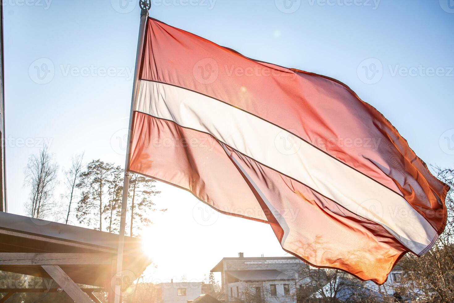 Latvian Flag Waving with Trees, Rooftops, and Wooden Structure photo