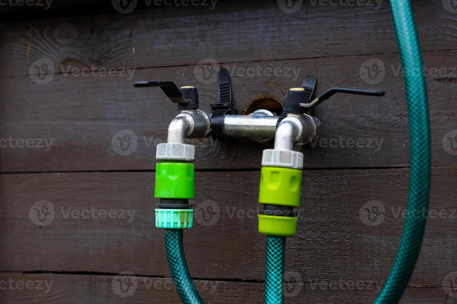 Outdoor Water Faucet with Dual Hose Connectors on Wooden Wall photo