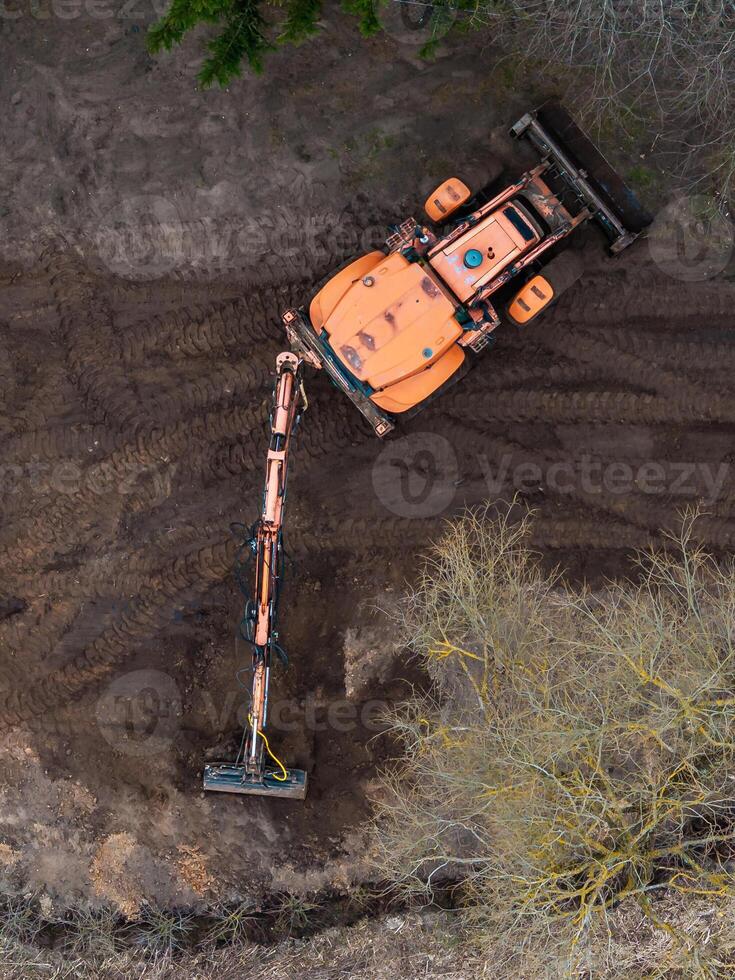 Aerial View of Orange Excavator on Dirt Surface with Sparse Vegetation photo