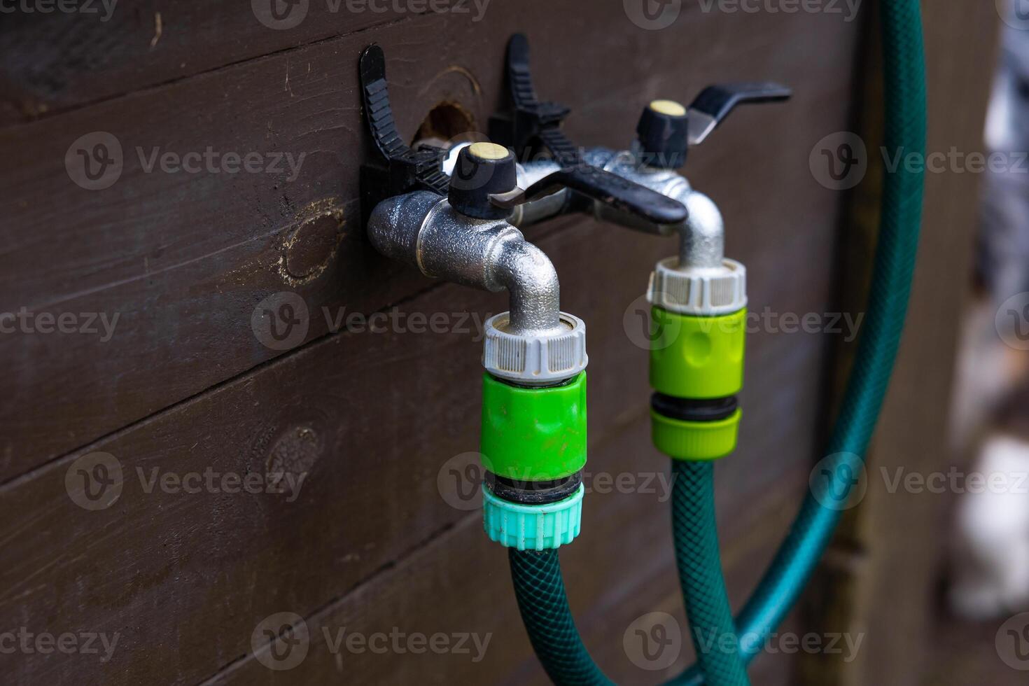 Outdoor Water Taps with Green Hose on Wooden Wall photo