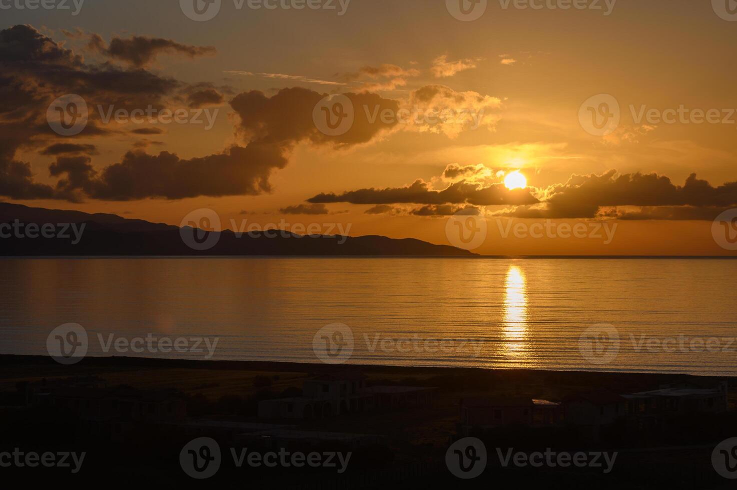 Golden sun sets over tranquil waters near distant mountains, casting serene reflections in the evening sky photo