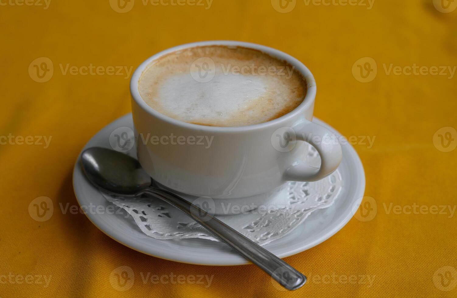 Warm cup of frothy beverage resting on a delicate lace doily atop a vibrant photo