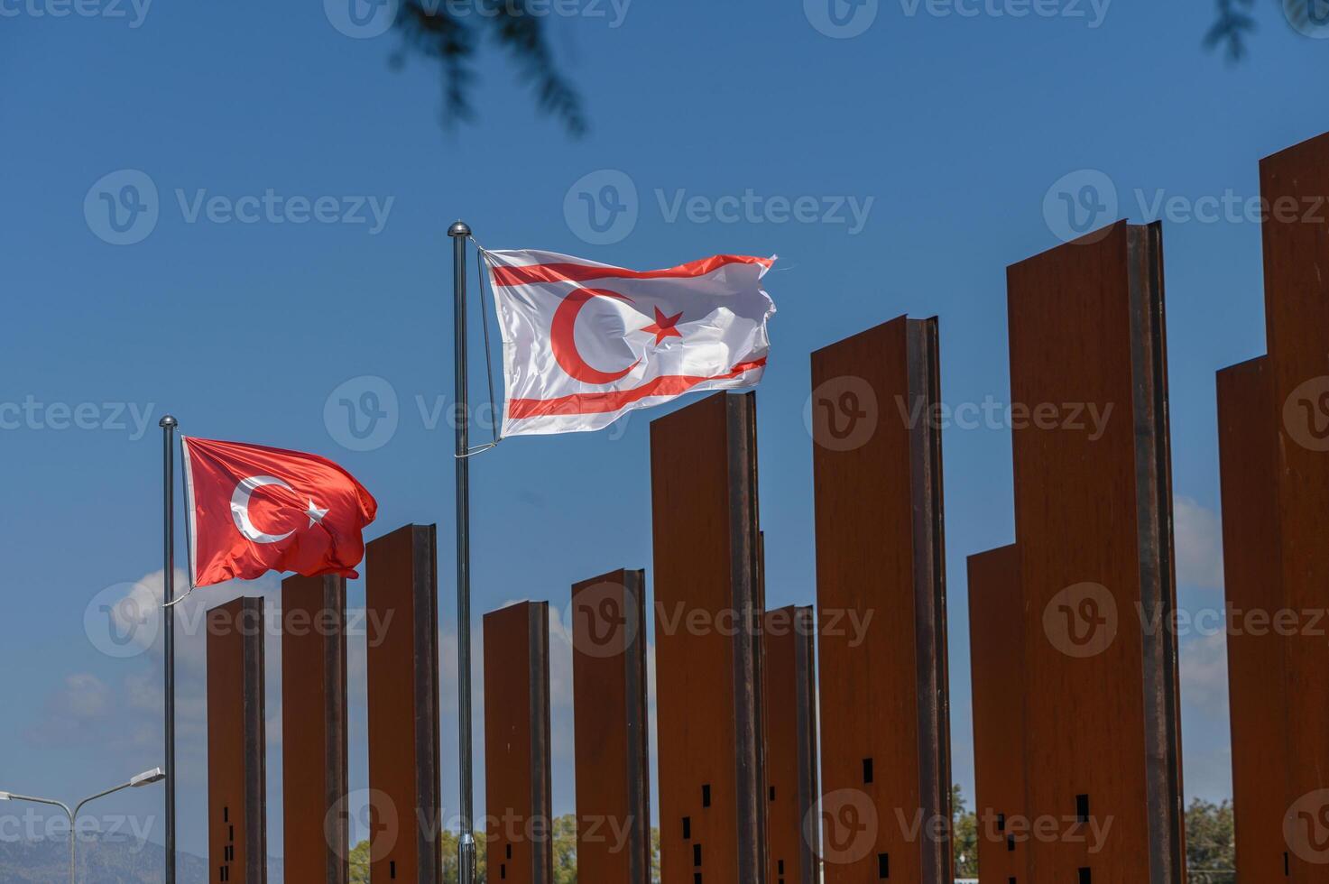 Waving flags of Turkey and Northern Cyprus celebrate unity against a backdrop of a blue sky and modern architecture during bright daylight photo