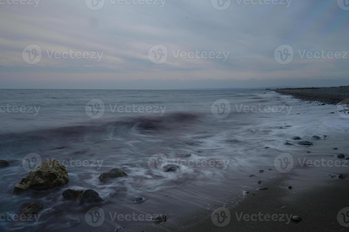 Waves gently caress pebbled shore under a twilight sky at a serene coastal location photo