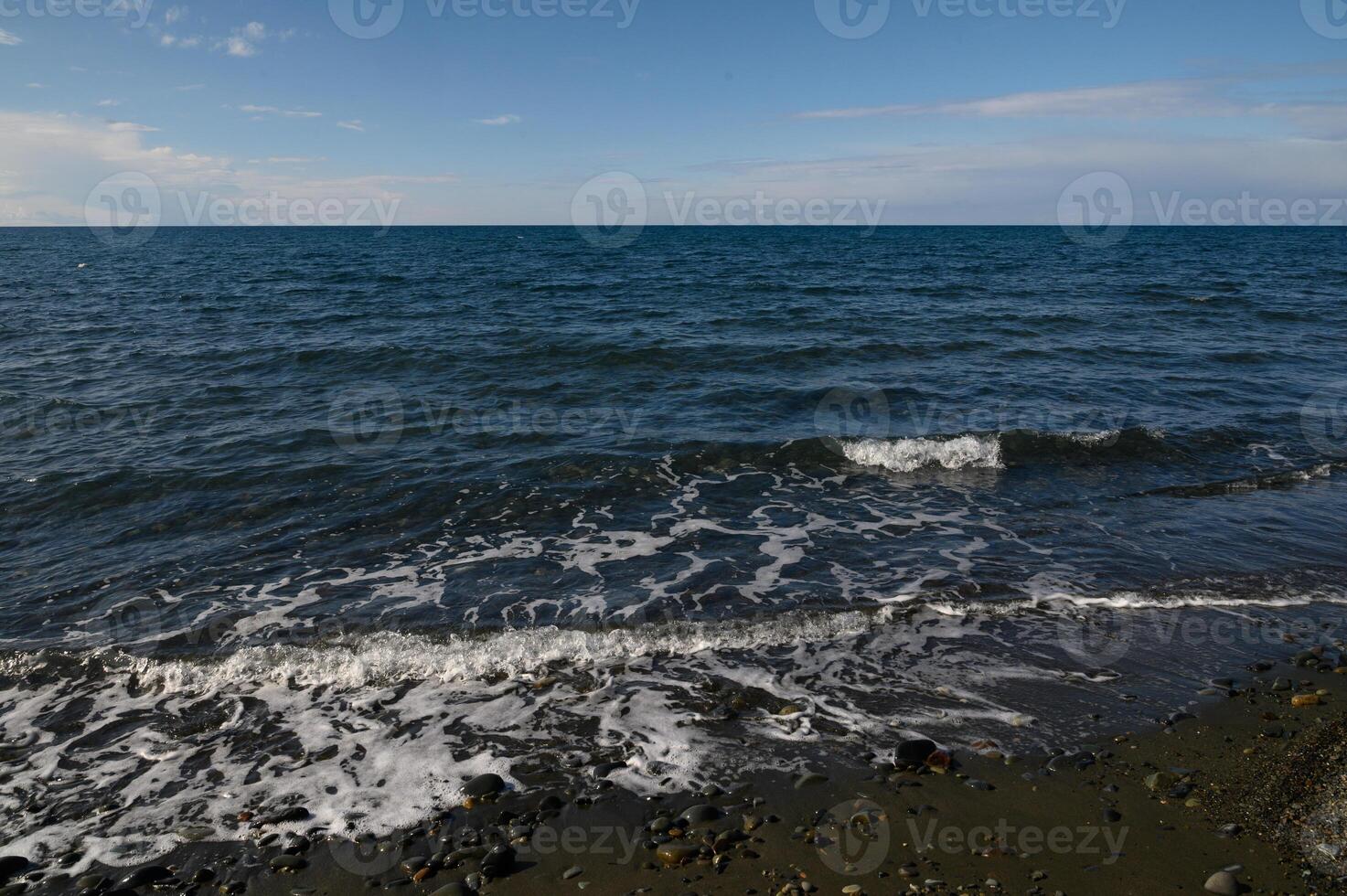Tranquil shoreline view with gentle waves lapping against pebbles in the afternoon sunlight photo