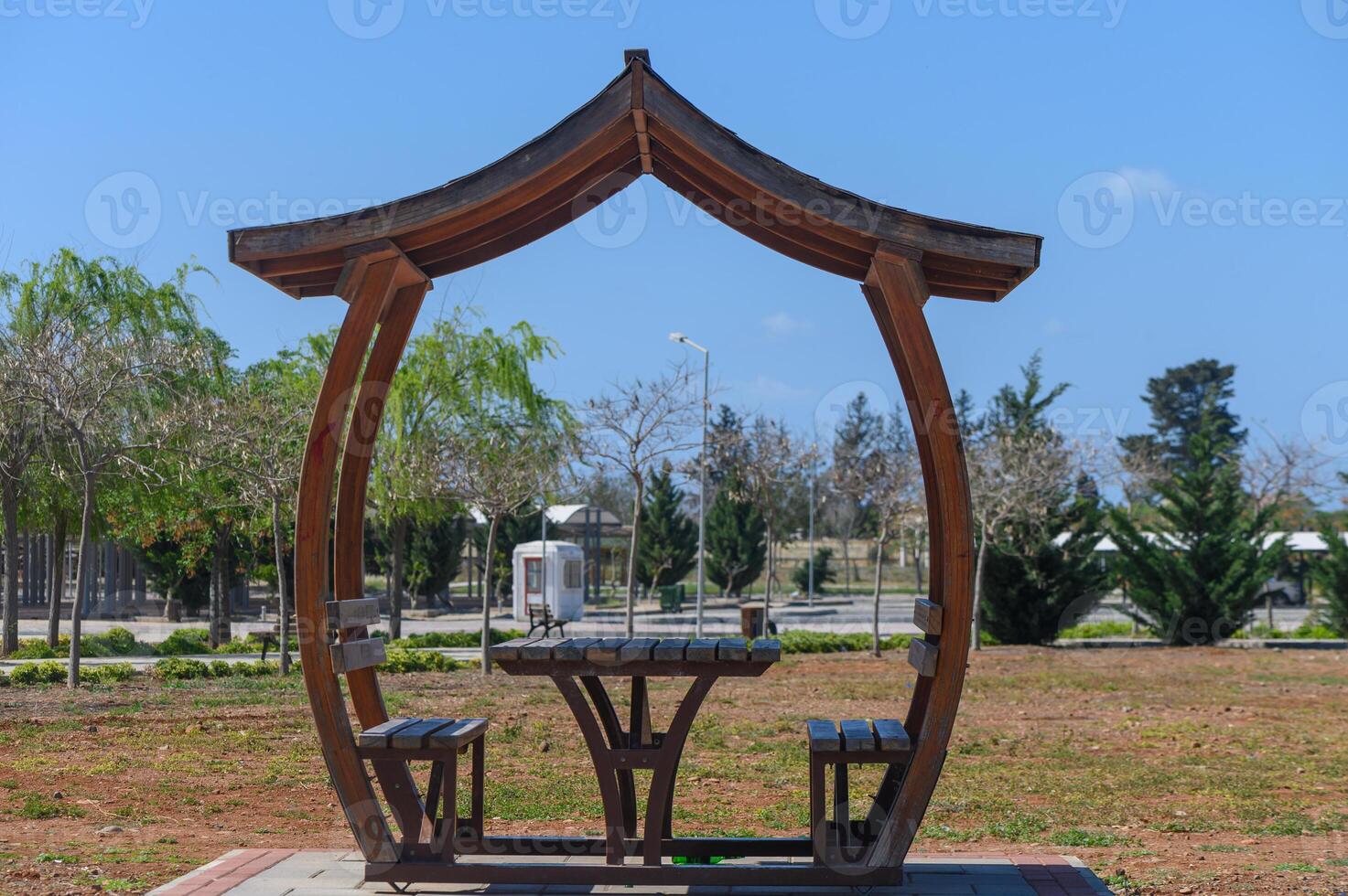Wooden structure in a sunny park provides a relaxing spot for rest and contemplation amidst beautiful greenery and clear skies photo