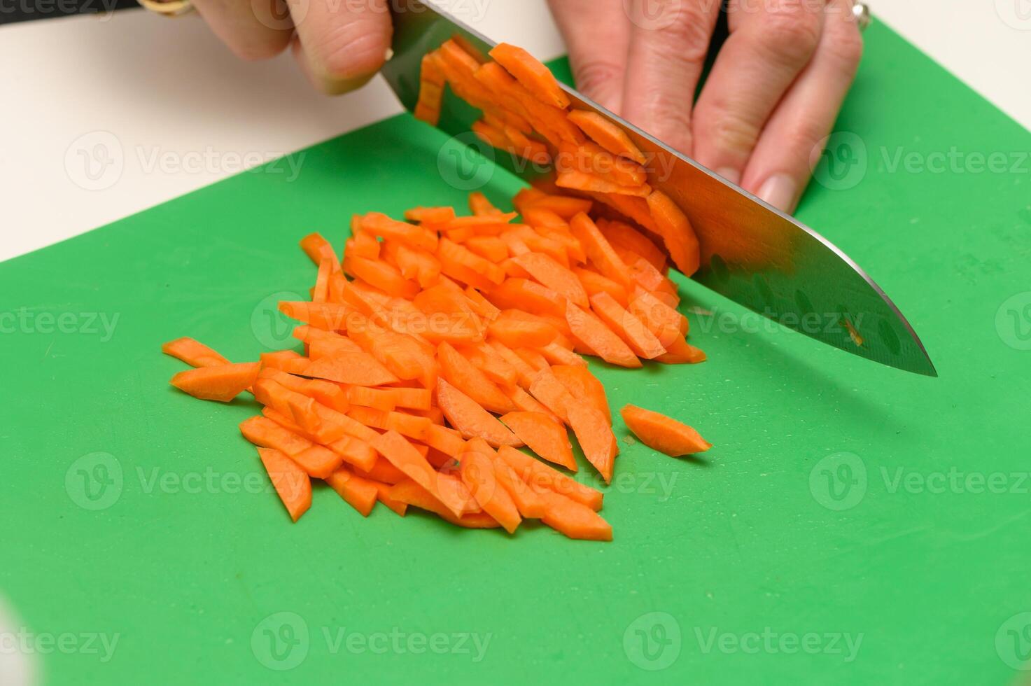 Hands skillfully slice vibrant orange carrots on a green cutting board, adding color to a culinary creation photo
