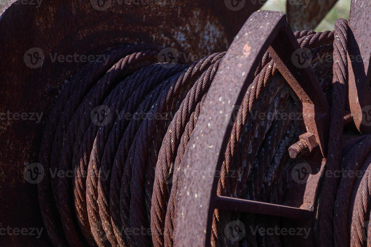 Rusty cable reel resting in the sunlight with a backdrop of serene nature on a clear afternoon photo