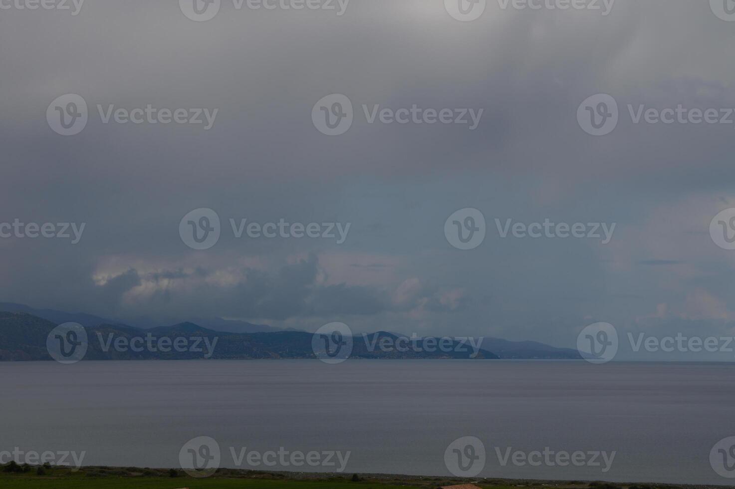 Skies over a tranquil coastal landscape capture the essence of a serene afternoon with dramatic clouds and still waters reflecting nature's beauty photo