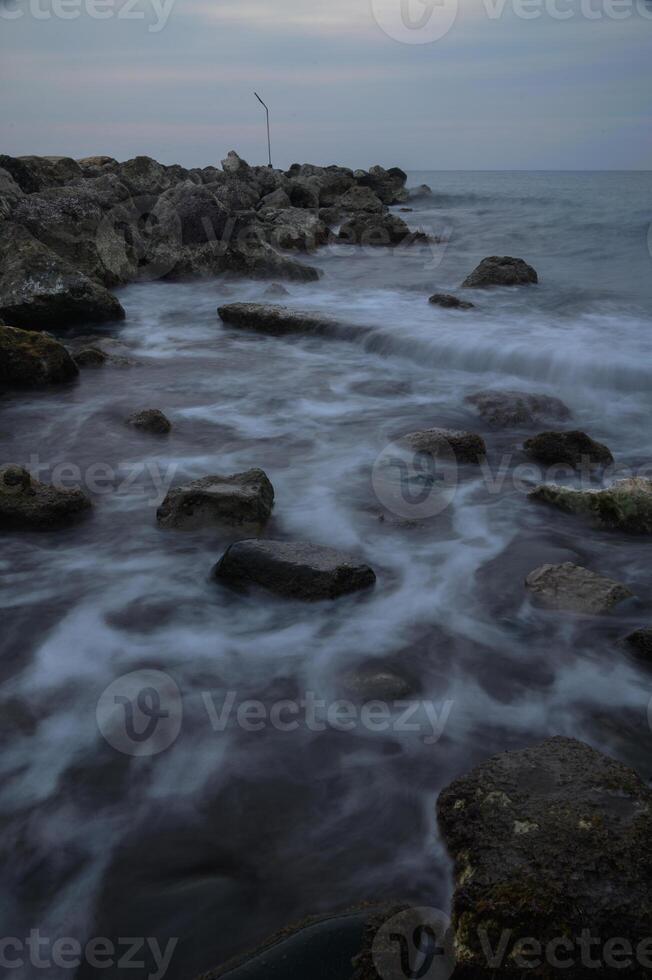 Waves gently caress the rocky shore at twilight, creating a mesmerizing dance of nature's elegance and beauty photo