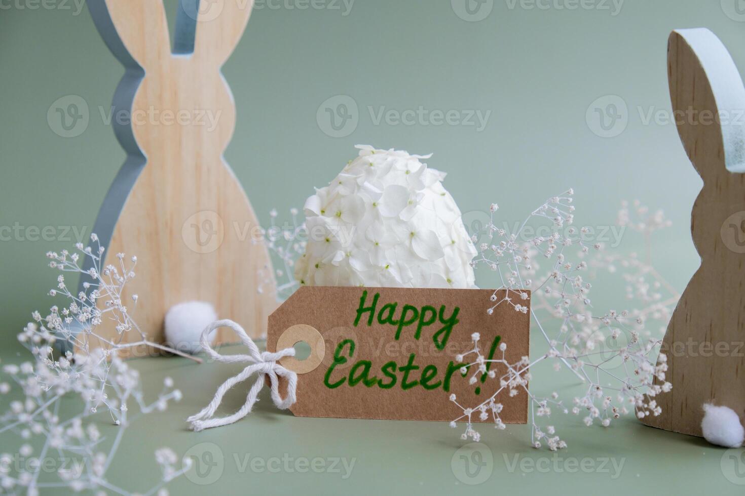 HAPPY EASTER paper note Wooden minimalism low-key bunny decor. Easter egg made of white lilac spring flowers in pastel green background. Sustainable holiday minimalistic still life composition. Wishes greeting card postcard photo