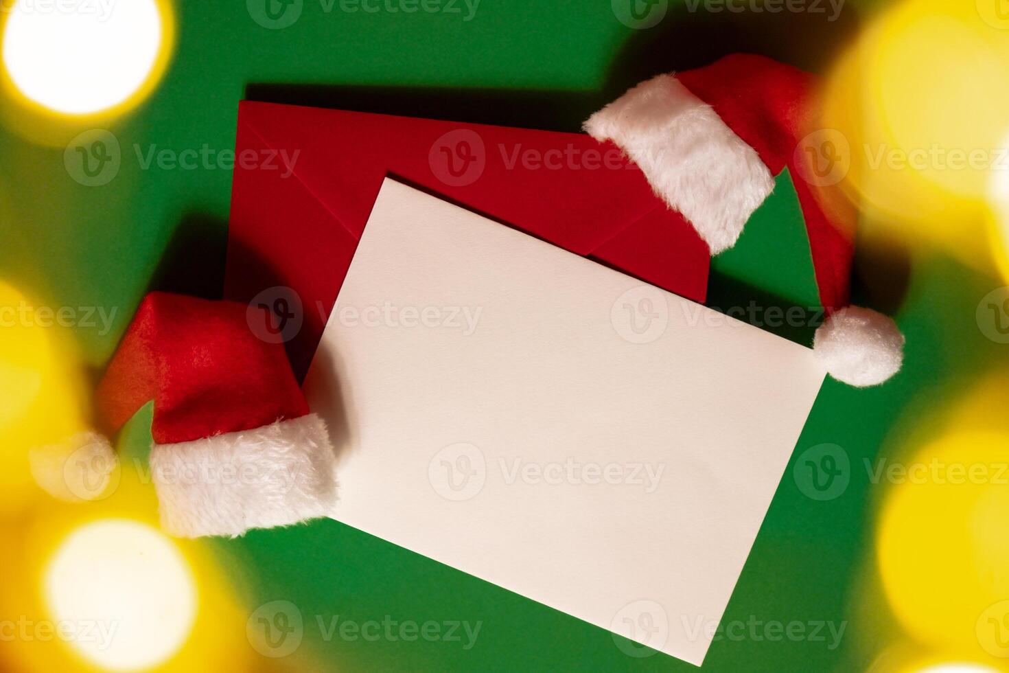 Santa hat with empty paper card note envelope on green background. Copy space for your text. Mock up for advertisement. Holiday Christmas composition. Minimalistic greeting card. Creative photo