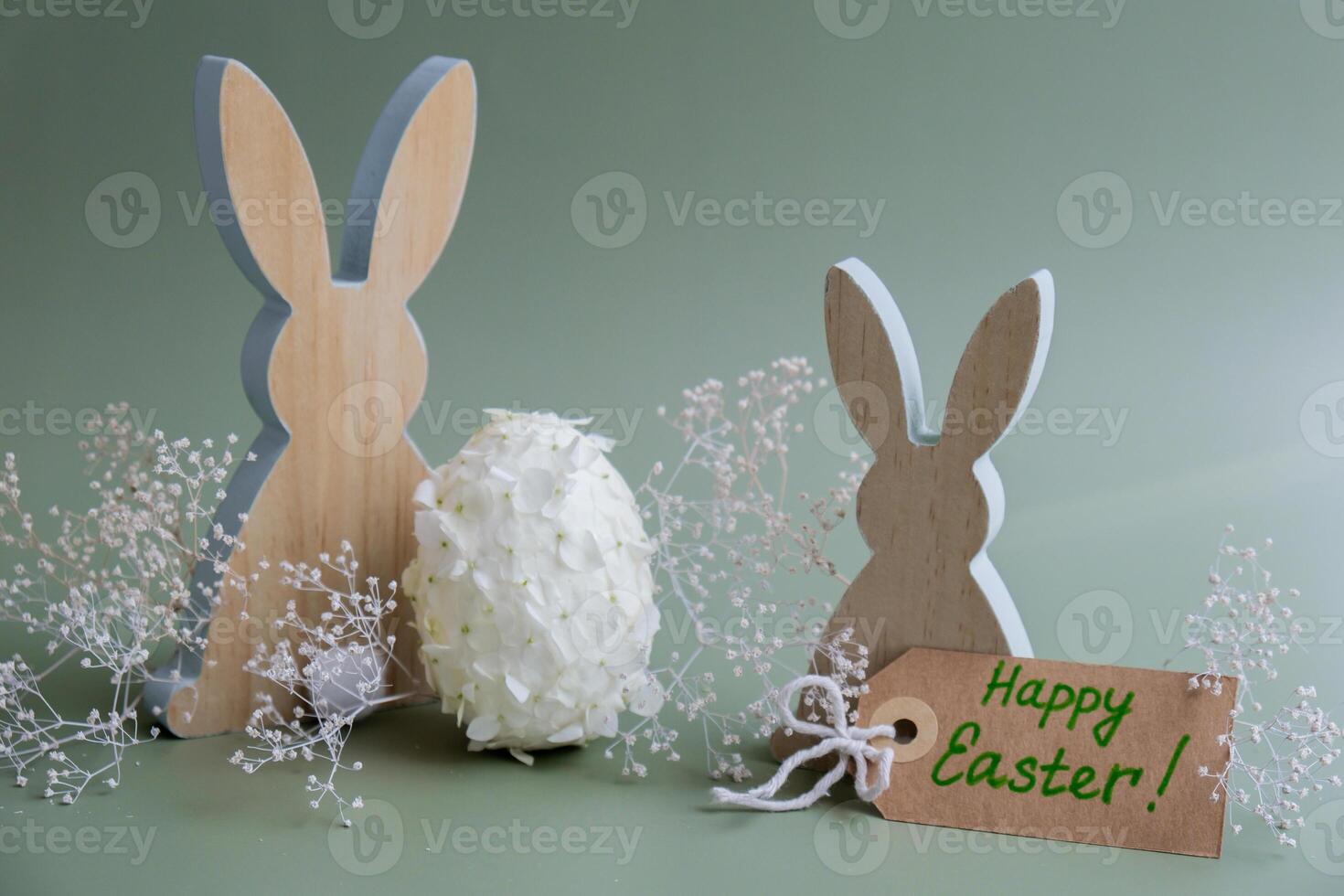 Greeting card with text HAPPY EASTER Creative Easter egg shape made of white lilac spring petals flowers. Responsible holidays decoration wooden rabbit bunny decor. Present gift idea Minimal holiday concept still life. Postcard photo