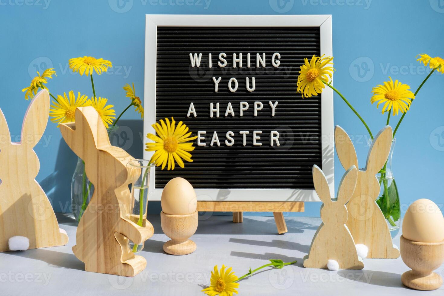 WISHING YOU A HAPPY EASTER text on letter board with bunny wooden figures and fresh flowers. Easter composition content still life. Christian symbols of spring holiday photo