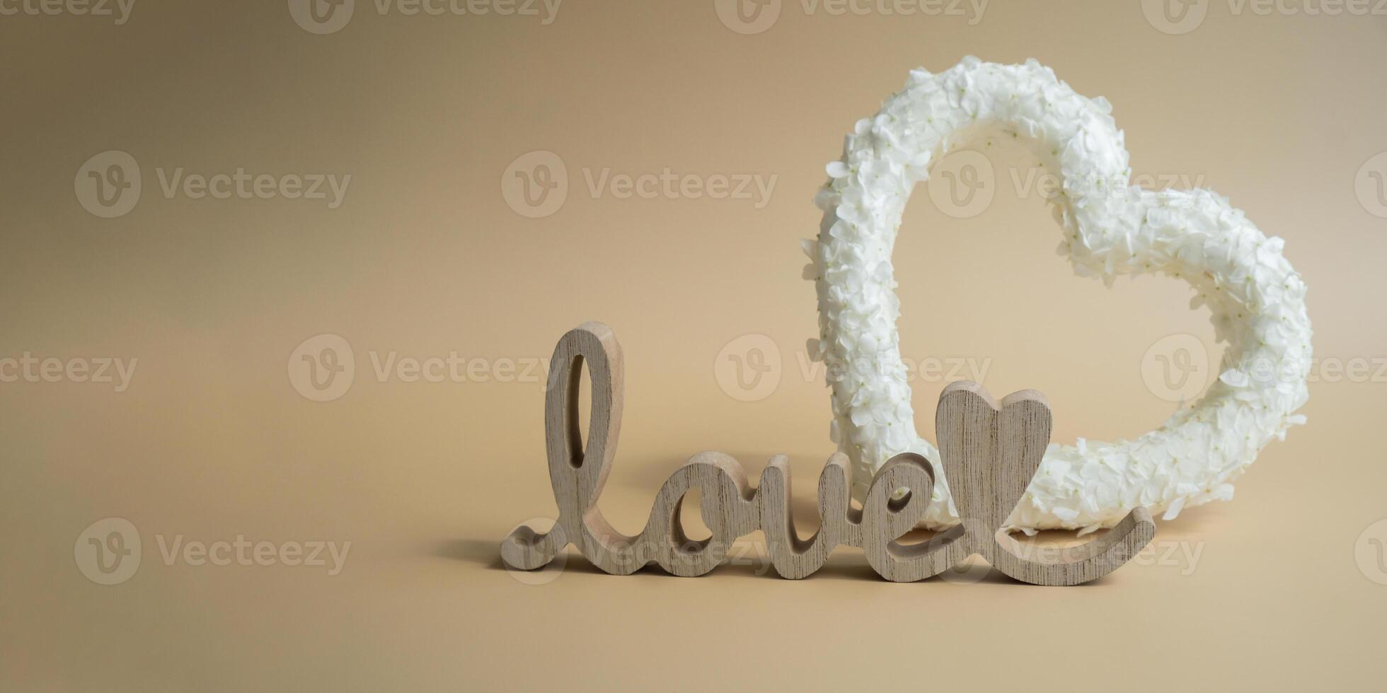Symbol of love beautiful flower petals in heart shape with Wooden word LOVE in beige background. Creative concept of St Valentines day, weeding romantic date or anniversary. Copy space greeting card photo