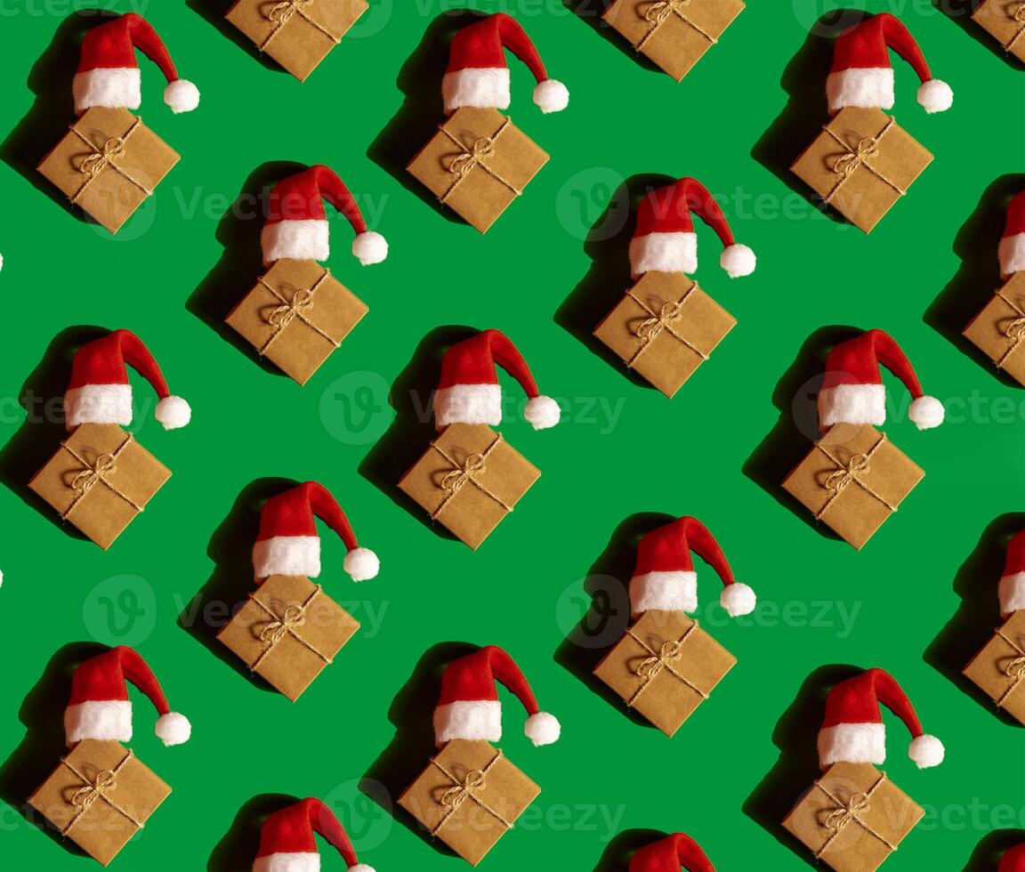 Pattern of Santa hat on paper gift box present on green background. Copy space for your text. Mock up for advertisement. Holiday Christmas texture composition. Minimalistic greeting card. Creative photo