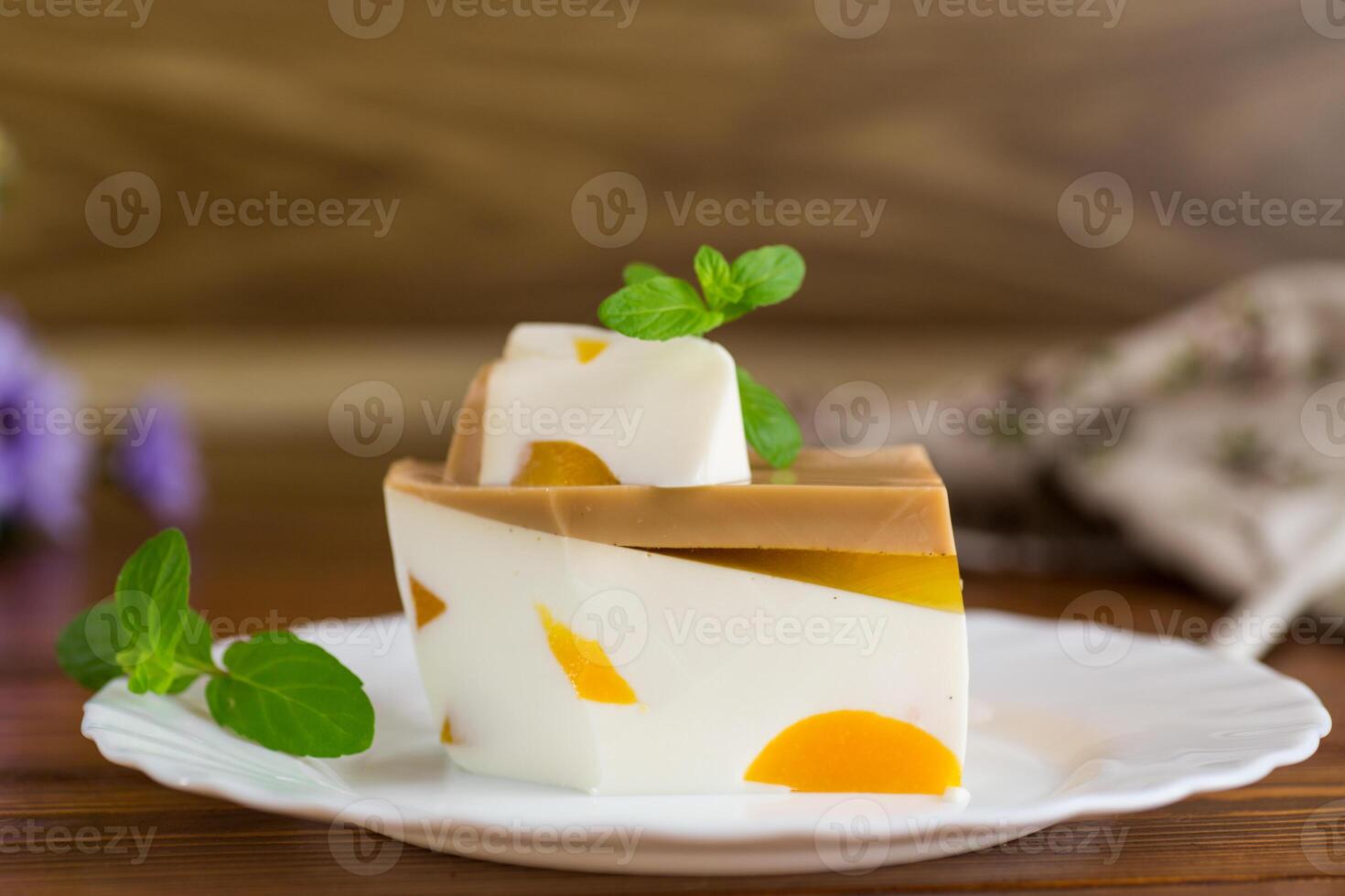 Jelly sweets.milk fruit jelly dessert with pieces of fruit inside, in a plate on a wooden table photo