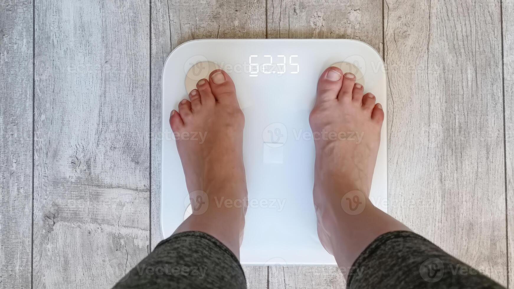 A person stands on a digital scale, revealing a measurement of 62.35 kg, suggesting a moment of self-reflection or weight tracking. photo