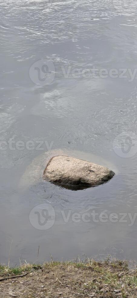 A solitary boulder partially submerged in calm water, showcasing natural rock formations and the beauty of a serene aquatic landscape. photo