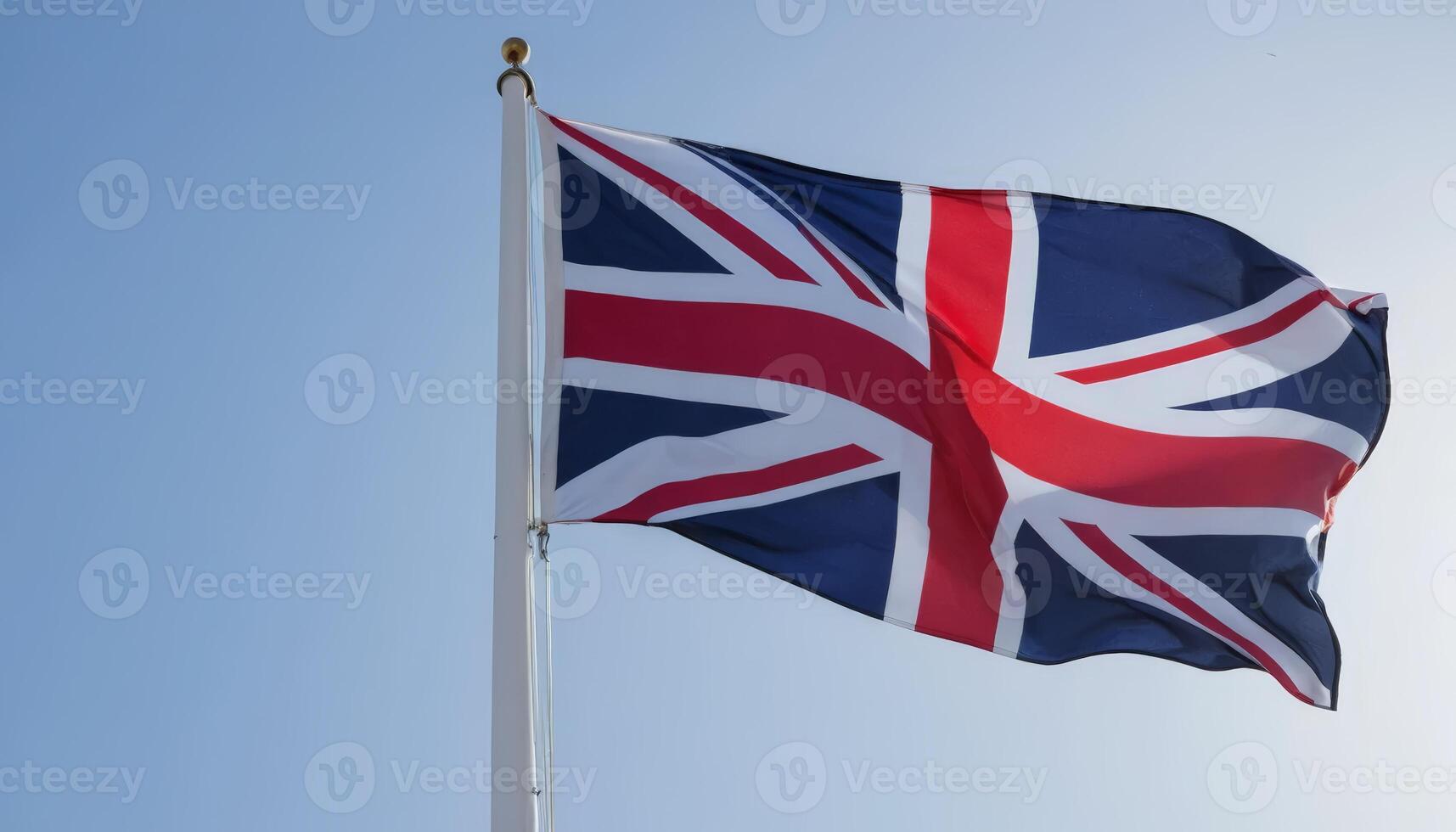 The Union Jack flutters prominently against a bright blue sky, embodying British history and pride with its distinctive red, white, and blue design. photo
