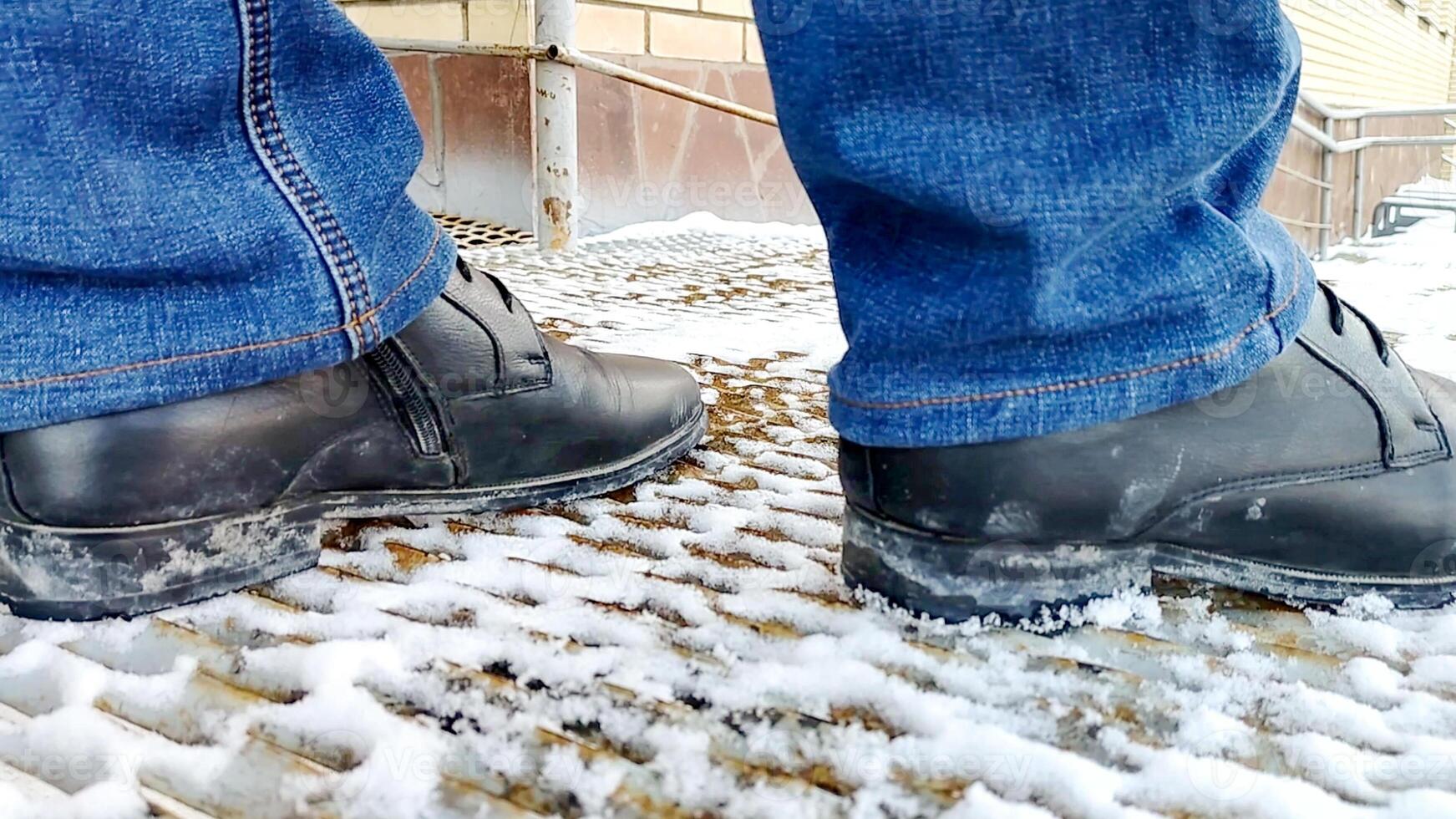 A person wearing black shoes standing on a snow covered sidewalk photo