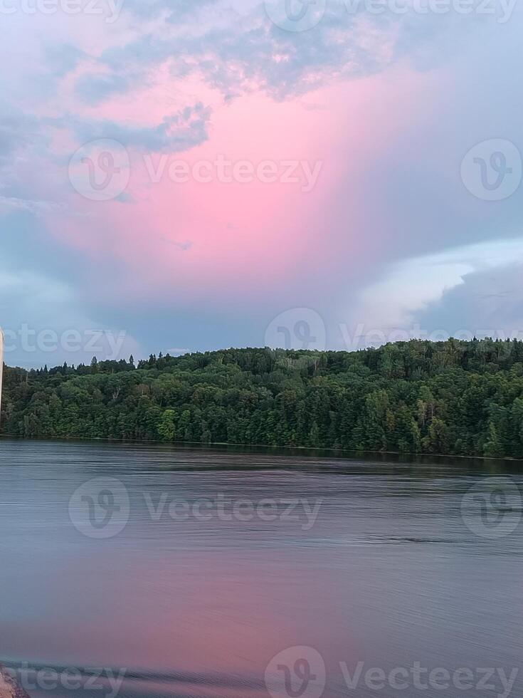 Beautiful pink sunset on a cloudy sky over the forest, along the riverbank photo