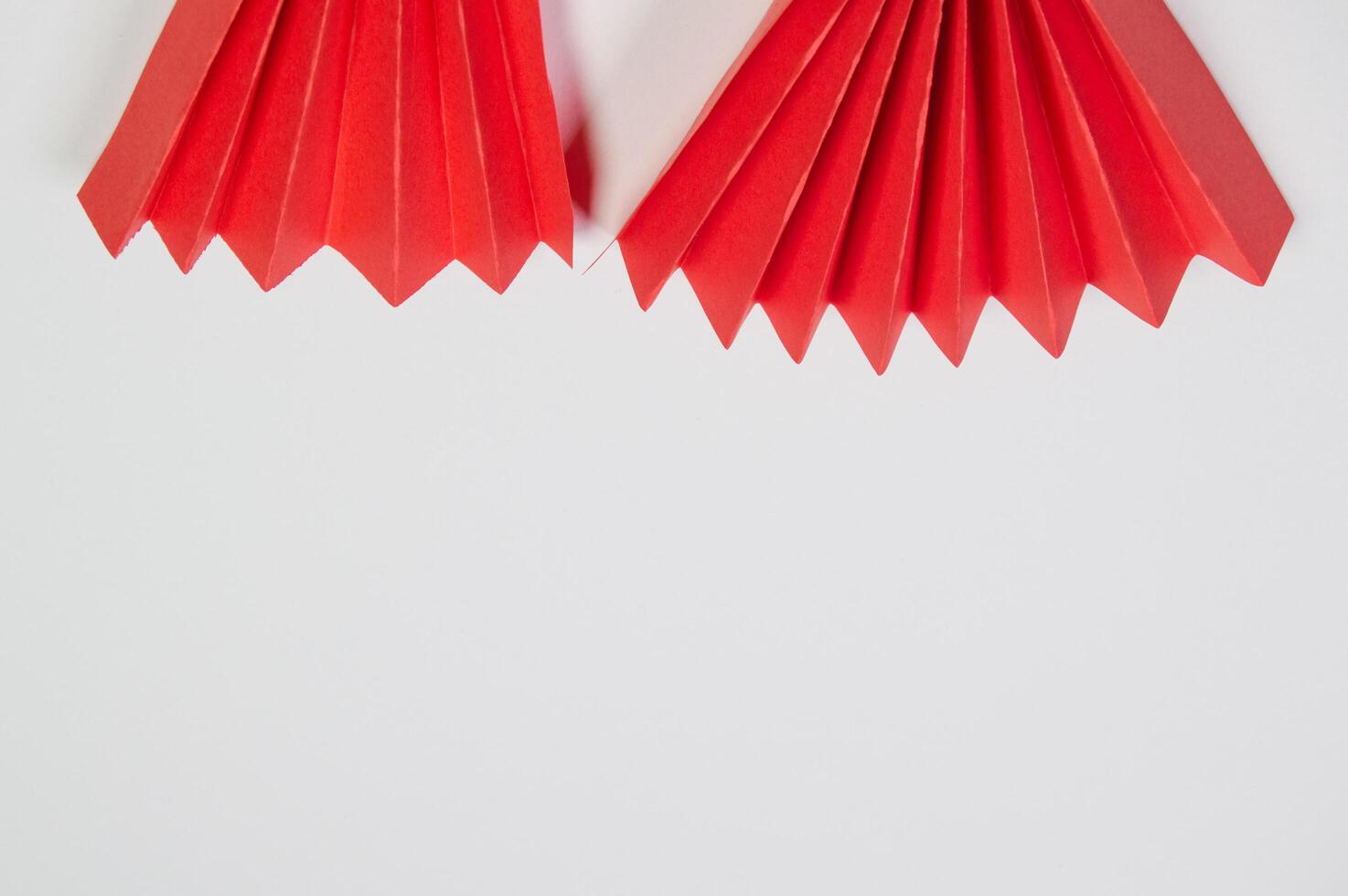 Two red origami fans are hanging from a white background photo