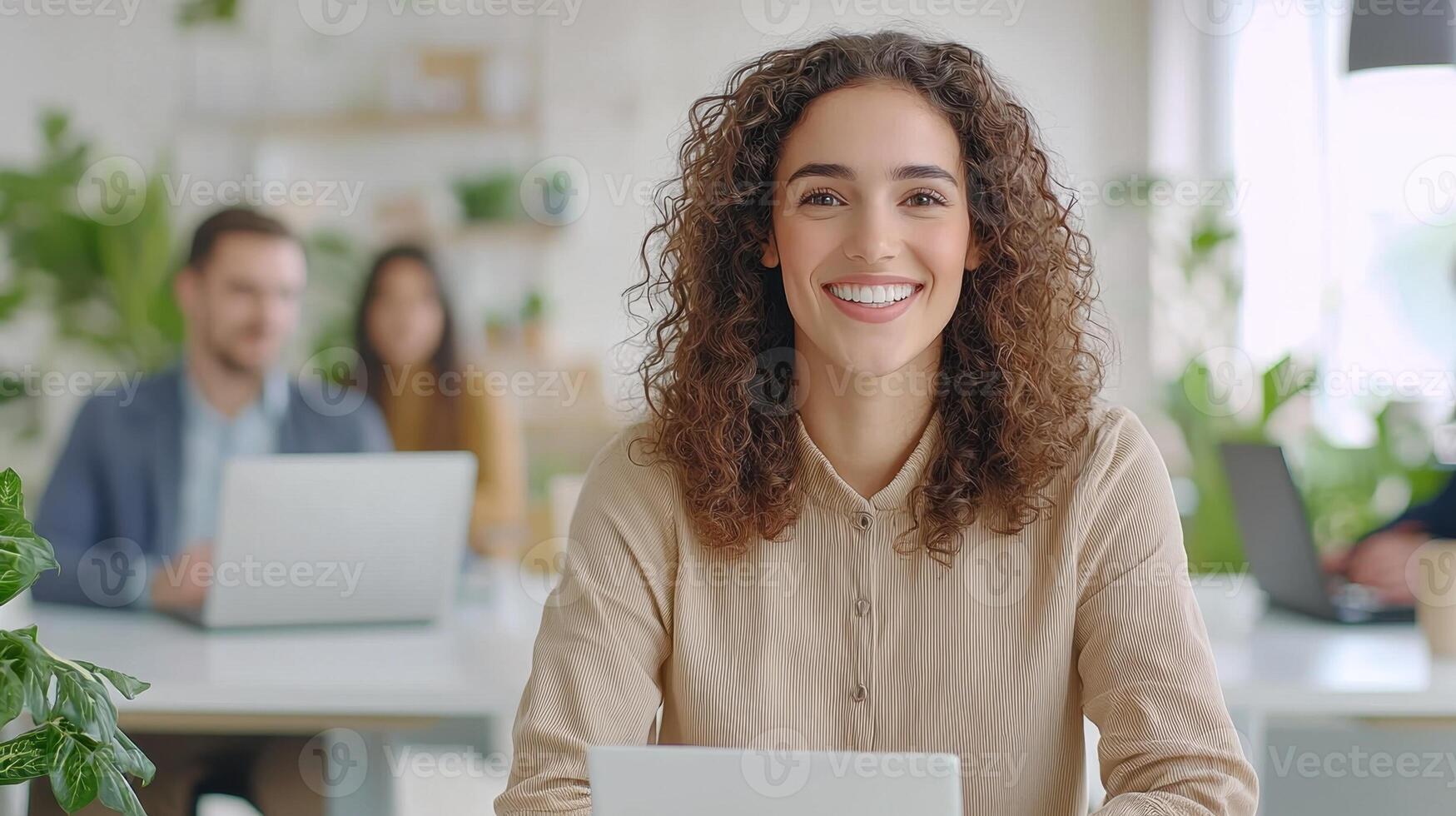 Portrait of a smiling businesswoman sitting at her desk with a laptop in a bright modern office, her colleagues are working in the background photo