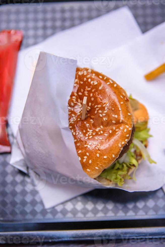 Top view of a delicious burger with sesame seed bun, fresh lettuce and tomato wrapped in paper, Closep of hamburger on the tray on the table in fast food restaurant. 2 photo