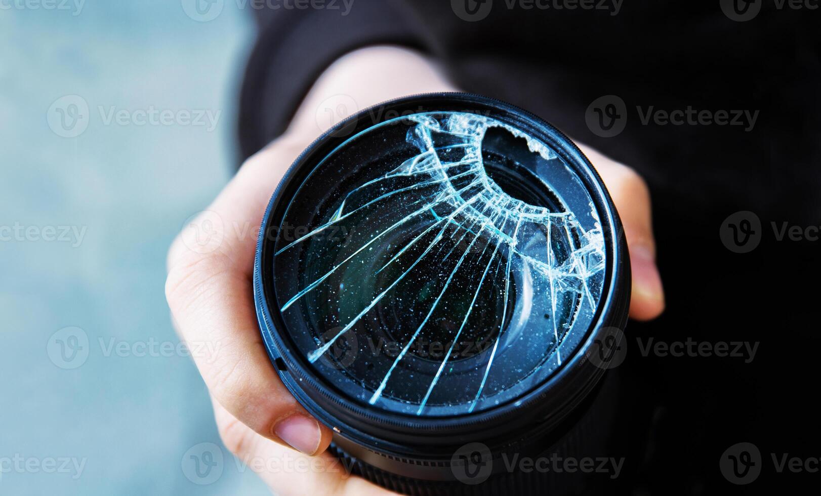 Closeup of a hand holding a broken shattered camera lens with visible cracks, symbolizing damage and fragility of photography equipment, repair or replacement needs, accidents, or fragility. 01 photo