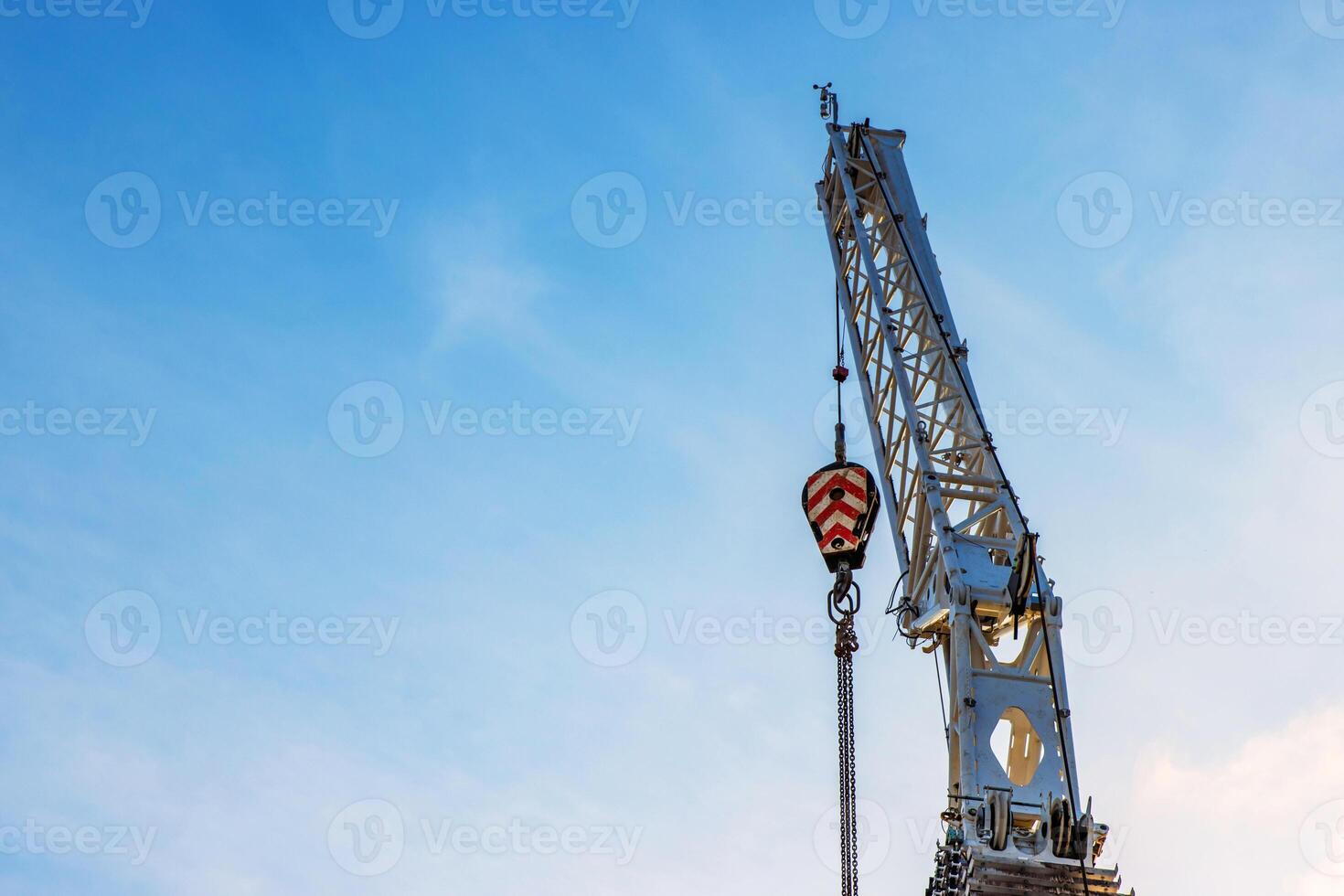 A large construction crane with cables extending against a clear blue sky, White crane arm and hanging cables captured from below, illustrating industrial work and heavy lifting. Copy space 02 photo