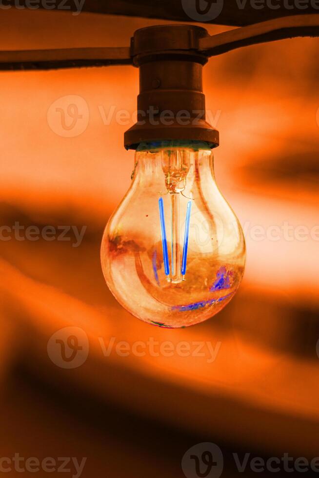 Orange glass bulb with socket on an orange background. Abstract concept image of colorful light lamp glowing against orange tones. innovation, technology, futuristic concept. Copy space photo
