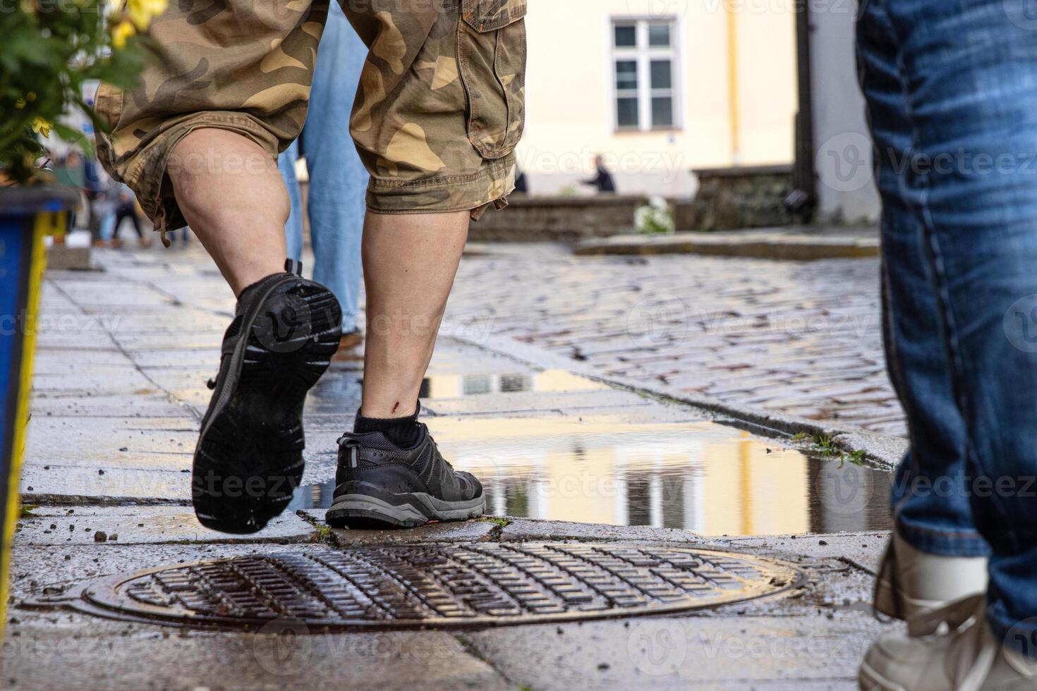 Closeup of men legs walking on a wet cobblestone street after rain, reflecting city architecture and urban lifestyle in Tallinn, Estonia, old town. Movement, footwear, rainy weather concept photo