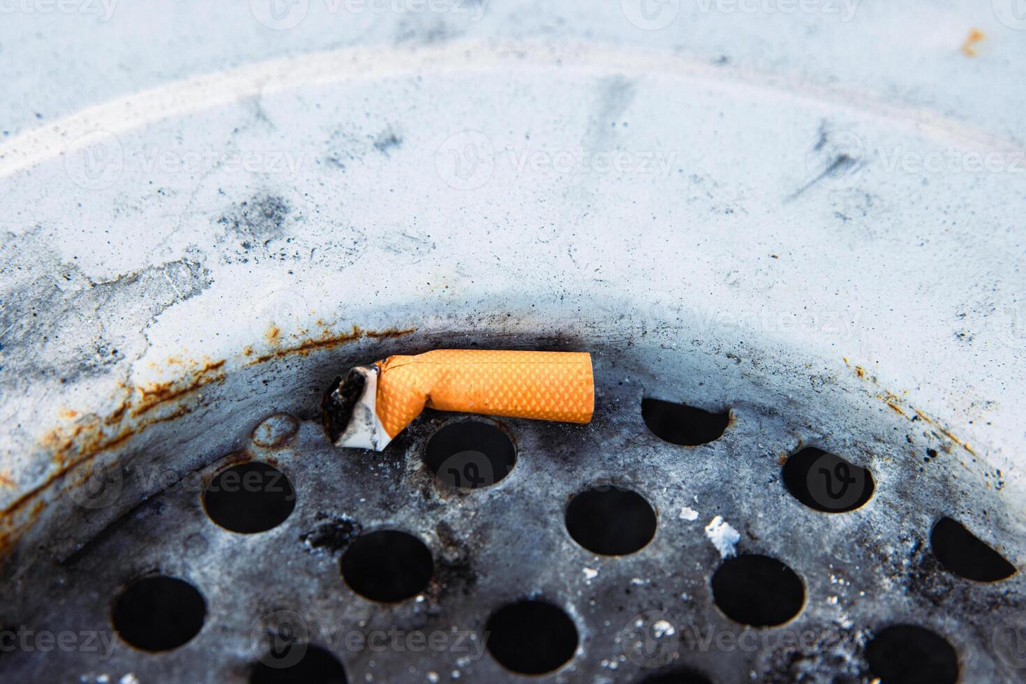 Closeup of a discarded cigarette butt stuck in a rusted metal grate of garbage bin. Nonsmoking, smoking harm, urban pollution, healthy and unhealthy lifestyle, littering, environmental concept. 2 photo