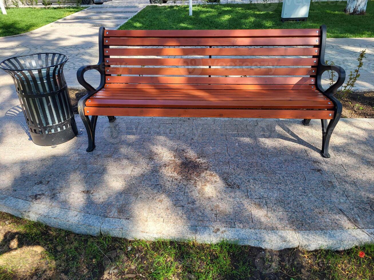 On a clear sunny spring day, there is a new urn and a brown bench in a shady park photo