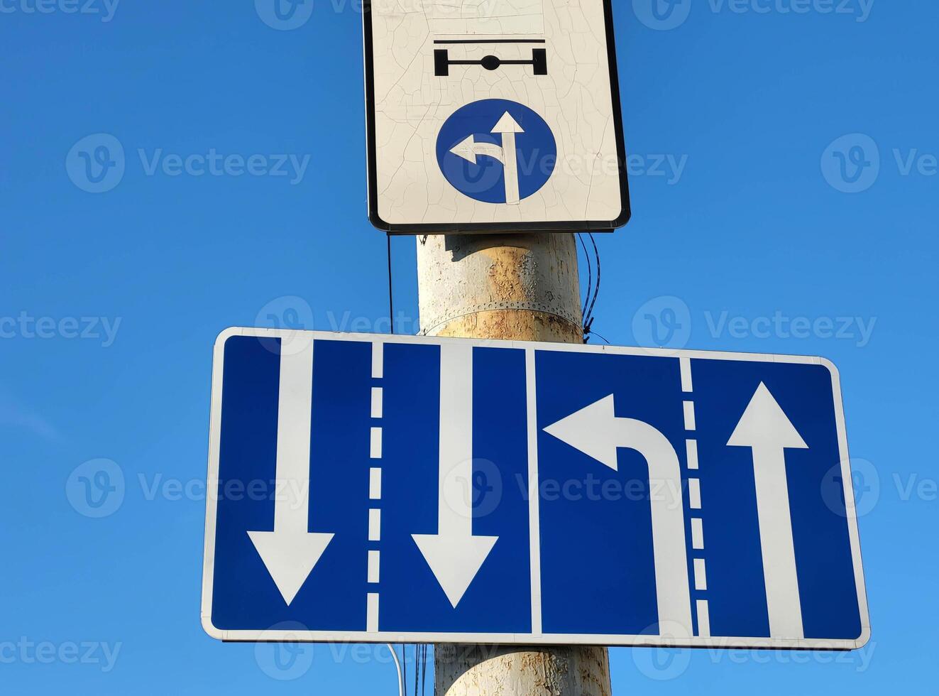 White arrows on a blue background are a standard road sign on a vertical pole against the sky photo
