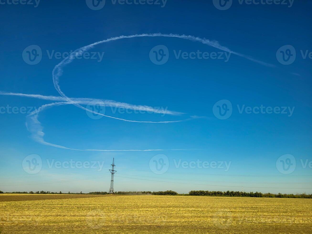 On the blue sky, a semicircular trace from an airplane over a field. photo