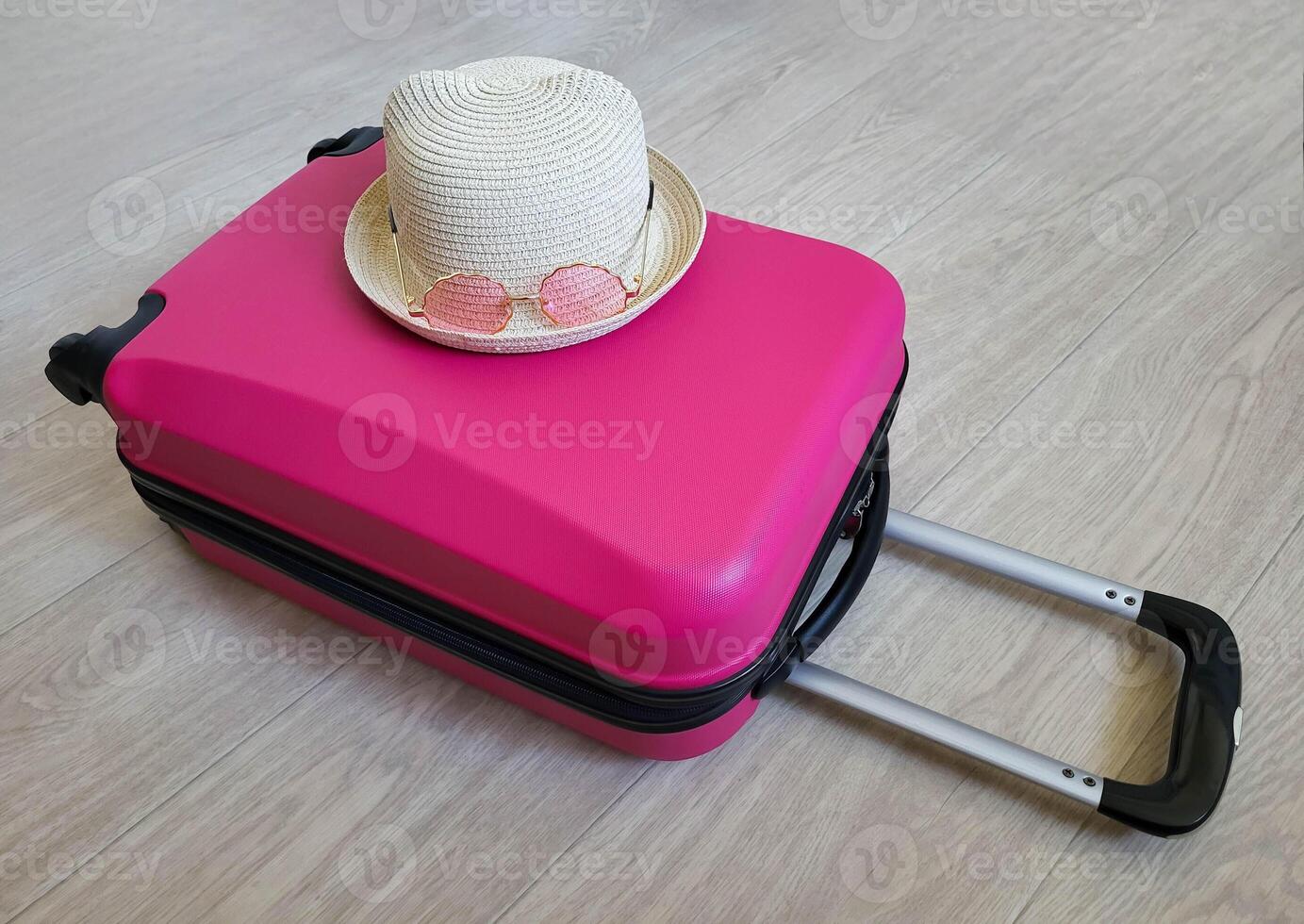 A child's hat and pink glasses are lying on a pink children's suitcase. The concept of children's recreation photo