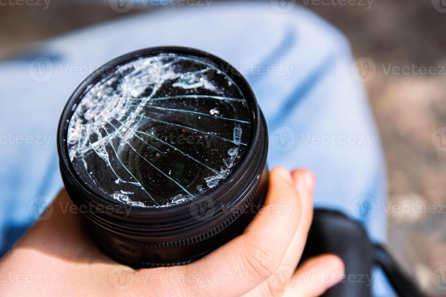 Closeup of a hand holding a broken shattered camera lens with visible cracks, symbolizing damage and fragility of photography equipment, repair or replacement needs, accidents, or fragility. 04 photo