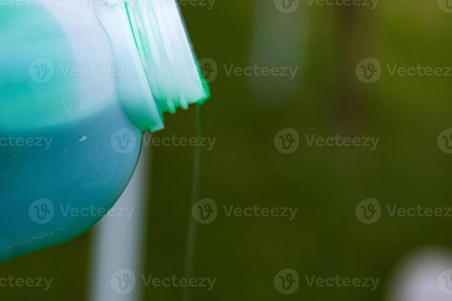 Closeup of vibrant green detergent pouring from a white plastic bottle against a blurred background. Green liquid flowing from a container. Copy space. Selective focus 01 photo