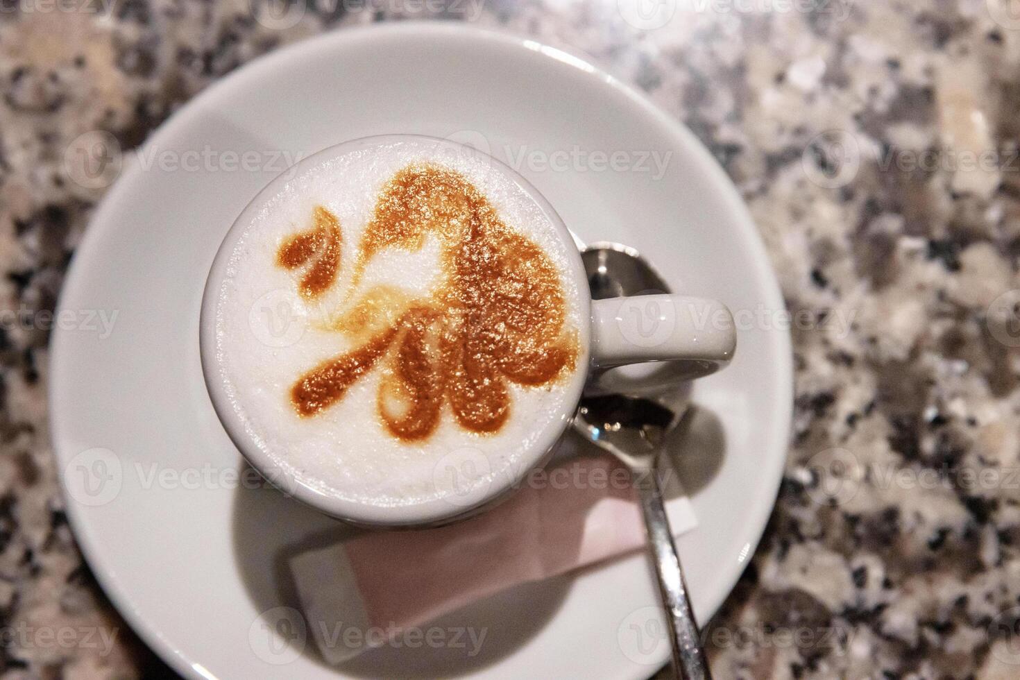 Top view of a cappuccino with intricate latte art in a white ceramic cup on a marble table, served with a spoon and sugar, Coffee culture, creativity, barista skills concept and cozy cafe 01 photo