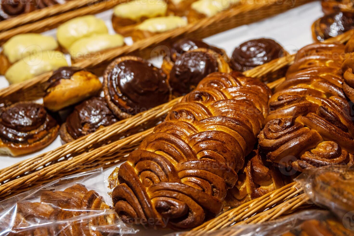 Assortment of freshly baked challah loaf and golden brown pastries with vanilla and chocolate toppings displayed in rustic woven wicker baskets on the shelf on grocery department in supermarket. 03 photo