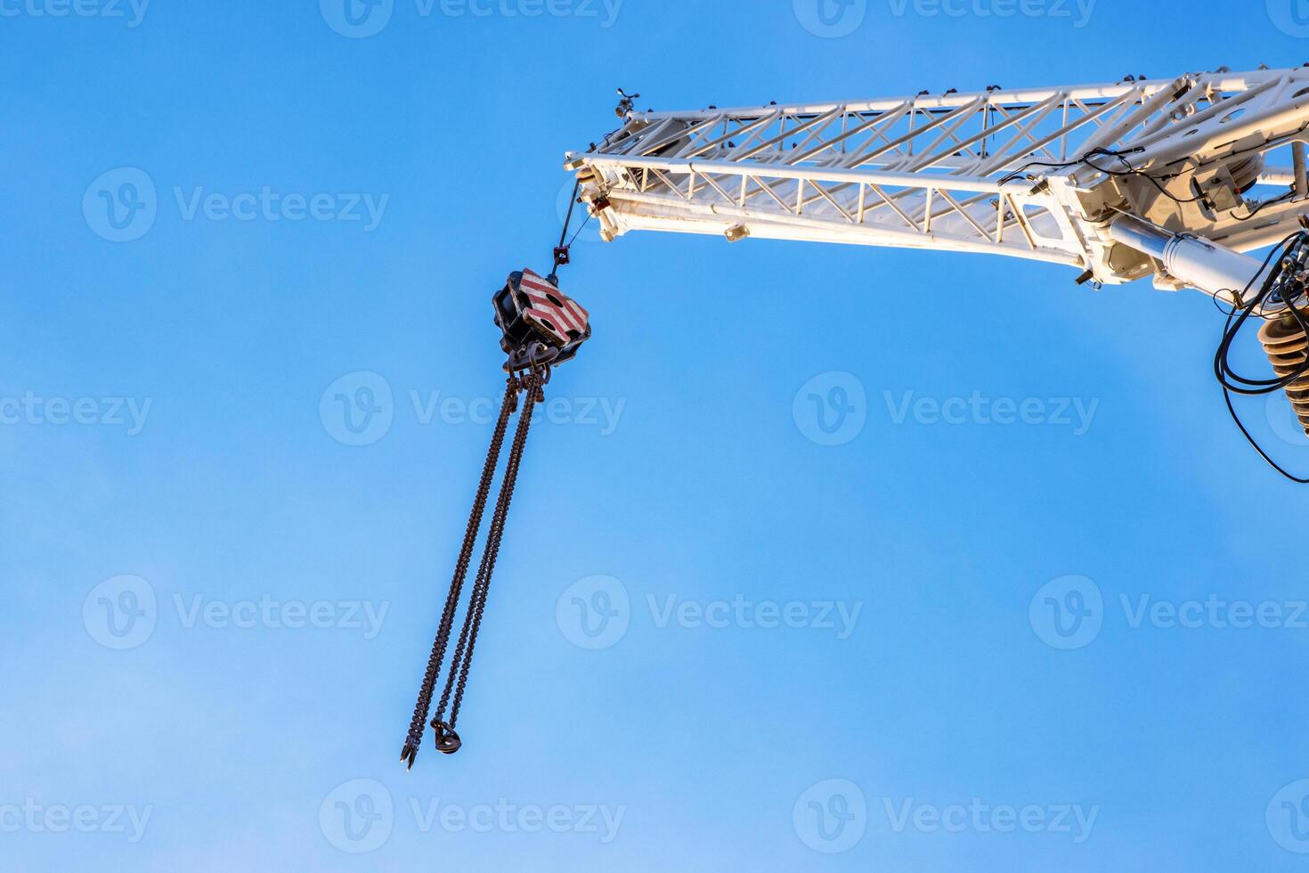 A large construction crane with cables extending against a clear blue sky, White crane arm and hanging cables captured from below, illustrating industrial work and heavy lifting. Copy space 01 photo