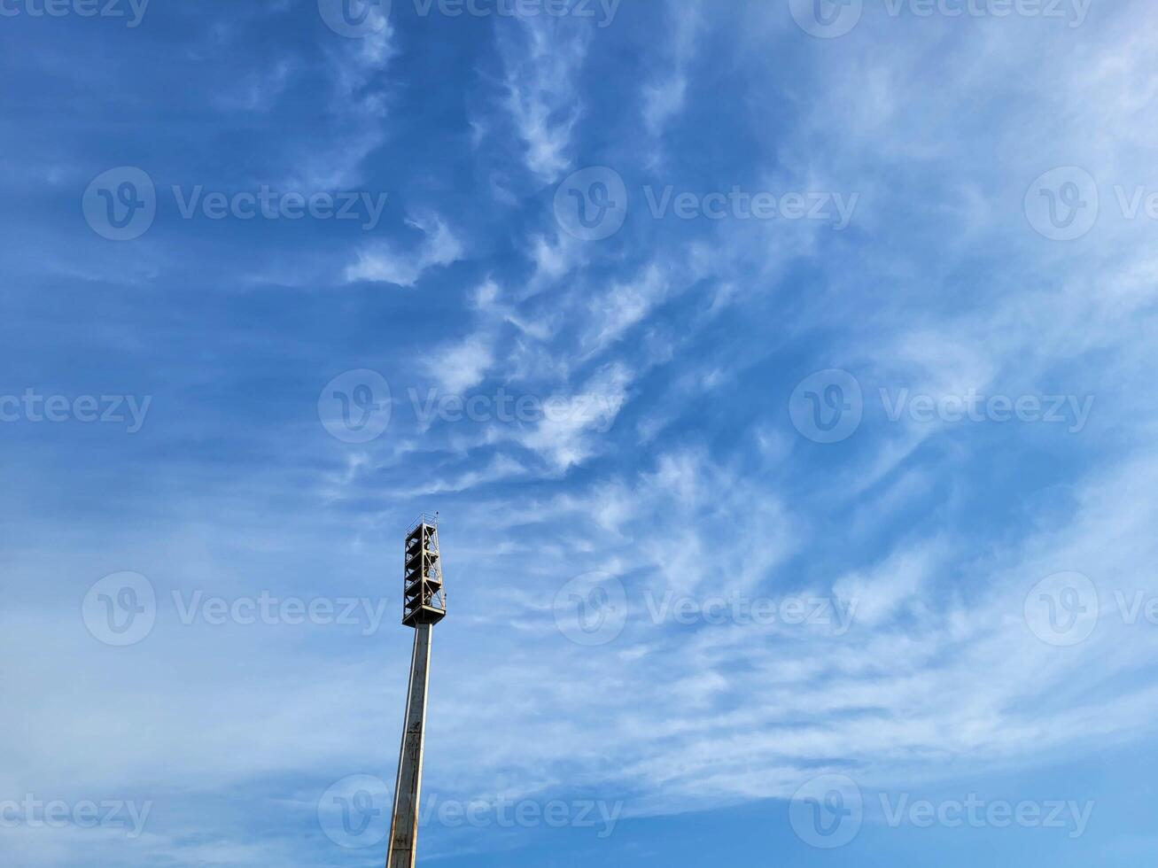 A searchlight lighting mast against the background of a blue sky with feathery clouds photo
