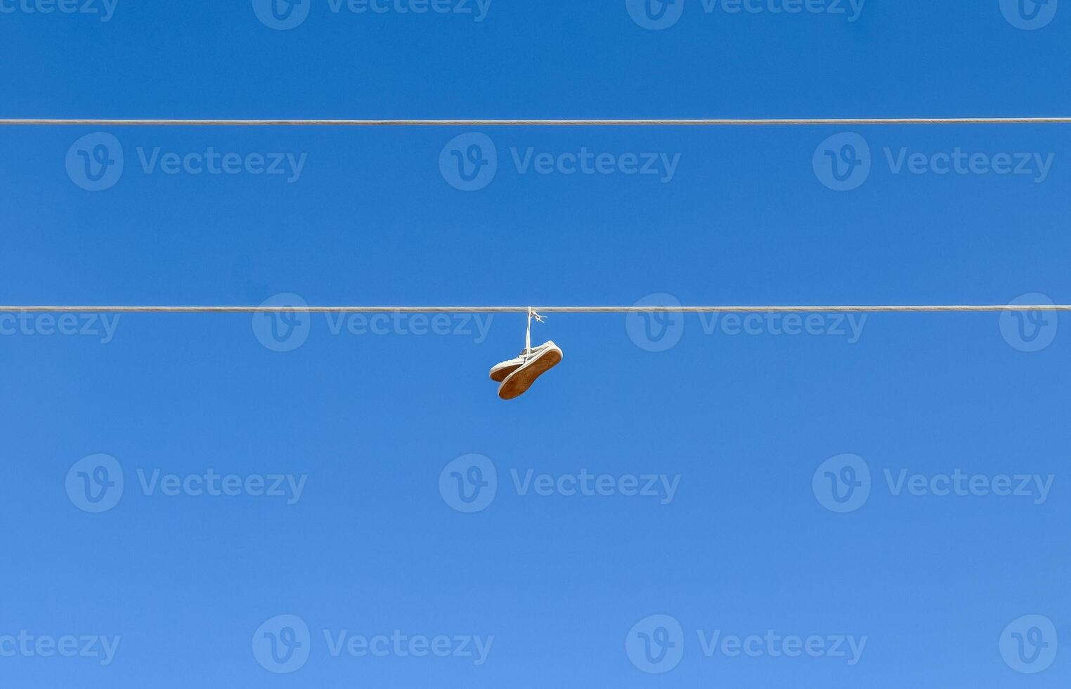 Pair of sneakers hanging from power line against blue sky photo